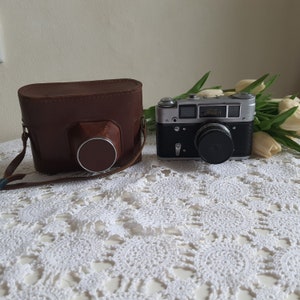 May include: A vintage silver camera with a brown leather camera case. The camera has a black lens and the text "FED" is visible on the front.