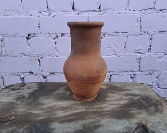 May include: A terracotta clay pitcher with a wide base and a narrow neck. The pitcher is brown and has a rough, textured surface.