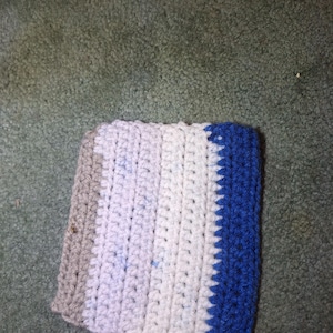 May include: A crocheted item with a color block design. The item features a gray section, followed by white, light blue, and a vibrant blue border. The handmade piece is likely a coaster or small mat.