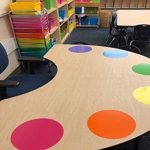 Pode incluir: Uma mesa de madeira clara com um design de paleta de pintura. A mesa tem oito círculos coloridos em tons de roxo, azul, verde, amarelo, laranja, vermelho e rosa.