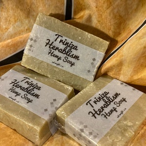 May include: Three bars of green soap wrapped in clear plastic with a white label that reads "Triniza Herablism Hemp Soap, net weight 1 oz."
