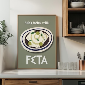 Könnte beinhalten: Ein gerahmter Druck mit hellgrünem Hintergrund. Der Druck zeigt einen Teller mit Feta-Käse und Oliven sowie den Text "Life's betta with FETA" in Weiß. Der Teller hat einen braunen und blauen Rand.