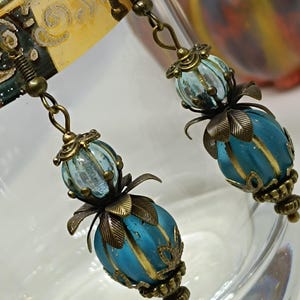 May include: A pair of dangle earrings with blue and gold glass beads and ornate bronze accents.