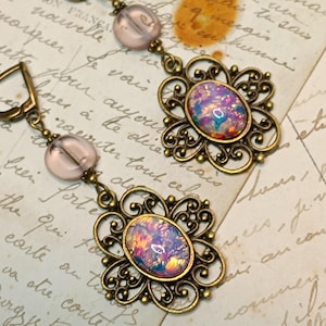 Peut inclure: Une paire de boucles d'oreilles avec un design délicat en filigrane et des pierres d'opale irisées. Les boucles d'oreilles sont en bronze et comportent des perles de verre roses.