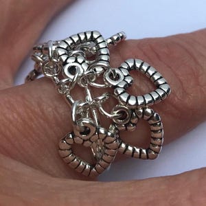 May include: A silver-toned bracelet featuring multiple heart charms. The bracelet has a toggle clasp and several dangling heart-shaped pendants. The hearts have a textured, beaded appearance. The bracelet is shown on a person's finger.