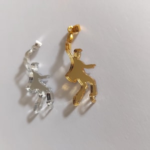 May include: Two mirrored acrylic pendants, one gold and one silver, shaped like a person dancing.