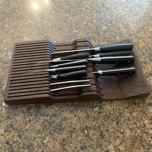 May include: A wooden knife block with a dark brown finish holds a set of eight knives with black handles. The knives are arranged in a staggered pattern, with the blades facing upwards.
