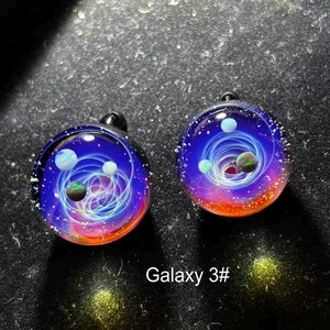 May include: Two glass pendants with a galaxy design. Each pendant features a swirling blue and white nebula with colorful planets and a red and orange gradient at the bottom. The text "Galaxy 3#" is at the bottom.