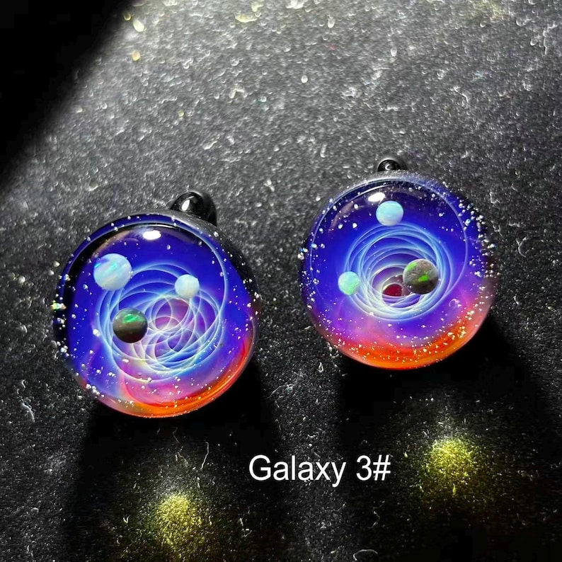 May include: Two glass pendants with a galaxy design. Each pendant features a swirling blue and white nebula with colorful planets and a red and orange gradient at the bottom. The text "Galaxy 3#" is at the bottom.