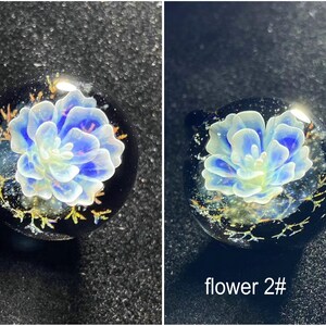 May include: Two round glass pendants with a blue and white flower design. The flower is encased in clear glass with a black background and gold accents. The text "flower 2#" is visible on one pendant.