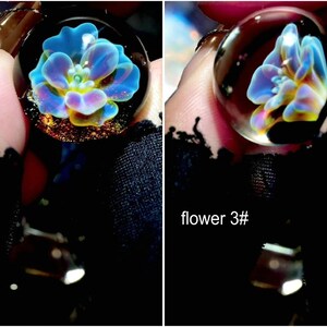 May include: A clear glass pendant with a blue, yellow, and purple flower design. The pendant is round and has a silver-colored bail. The text "flower 3#" is visible in the image.