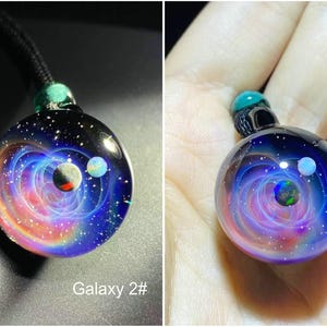 May include: A galaxy-themed glass pendant necklace. The round pendant features a swirling nebula design in shades of blue, purple, and orange, with three planet-like orbs. The pendant is attached to a black cord with a green bead.
