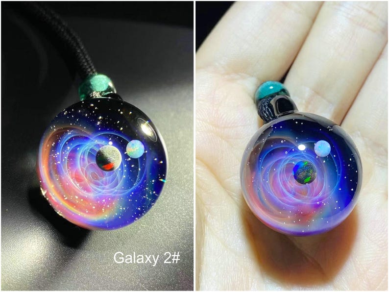 May include: A galaxy-themed glass pendant necklace. The round pendant features a swirling nebula design in shades of blue, purple, and orange, with three planet-like orbs. The pendant is attached to a black cord with a green bead.