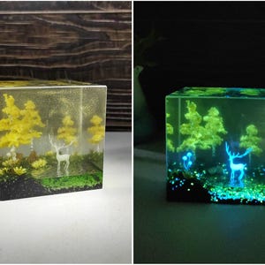 Puede incluir: Un cubo de resina transparente con una escena de bosque en miniatura. La escena incluye &aacute;rboles amarillos, un ciervo blanco y una base verde. El cubo brilla en verde en la oscuridad, con el ciervo y los &aacute;rboles iluminados.