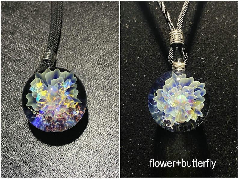 May include: A round glass pendant necklace with a flower and butterfly design. The pendant features a blue and white flower with iridescent accents, suspended within a clear glass orb. The necklace has a black cord.