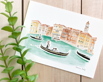 May include: Watercolor painting of a canal in Venice, Italy. The painting features colorful buildings lining the canal, with gondolas floating on the water. The text "Venice, Italy" is written in the bottom right corner.