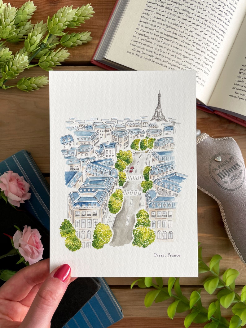 K&ouml;nnte beinhalten: Ein Aquarellgem&auml;lde einer Stra&szlig;enszene in Paris, Frankreich. Das Gem&auml;lde zeigt eine Stra&szlig;e, die von Geb&auml;uden, B&auml;umen und einem roten Auto ges&auml;umt ist. Der Eiffelturm ist in der Ferne sichtbar. Das Gem&auml;lde ist mit "Paris, Frankreich" signiert.