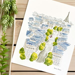 Puede incluir: Pintura a la acuarela de Par&iacute;s, Francia, que presenta una escena callejera con edificios, &aacute;rboles y la Torre Eiffel. La obra de arte tiene una combinaci&oacute;n de colores azul claro y blanco, con un coche rojo en la carretera. La pintura est&aacute; sobre papel blanco.