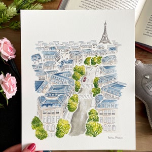 Puede incluir: Pintura a la acuarela de Par&iacute;s, Francia, con la Torre Eiffel y edificios de la ciudad con tejados azules. Una carretera con un coche rojo serpentea por la ciudad, bordeada de &aacute;rboles verdes. El texto "Paris, France" est&aacute; en la parte inferior.