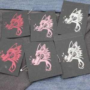 May include: Five rectangular black fabric patches featuring a screen-printed graphic of a wolf head in profile. Two patches display a red wolf design, two feature a light pink wolf design, and one patch shows a white wolf design with sharp teeth.