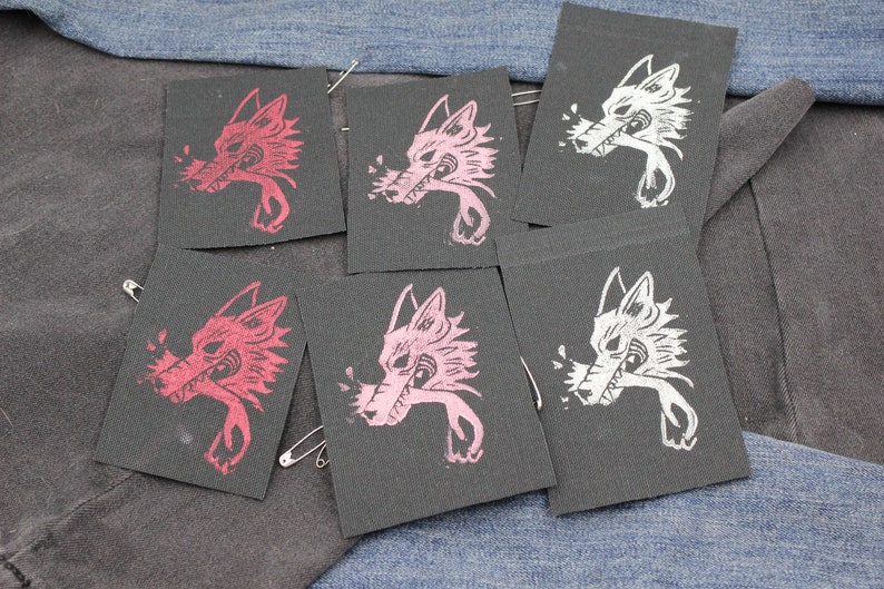 May include: Five rectangular black fabric patches featuring a screen-printed graphic of a wolf head in profile. Two patches display a red wolf design, two feature a light pink wolf design, and one patch shows a white wolf design with sharp teeth.