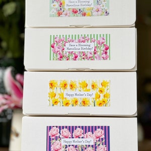 May include: Four white boxes with floral designs and text. The top two boxes have green and white floral designs with the text "Have a Blooming Marvellous Birthday!" The bottom two boxes have yellow and white floral designs with the text "Happy Mother's Day!" and pink and purple floral designs with the text "Happy Mother's Day!"