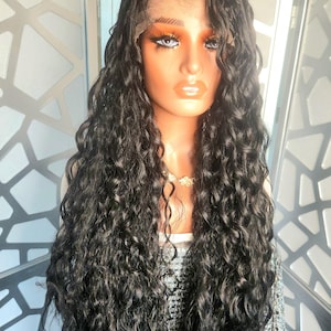 May include: A mannequin head with a long, wavy black wig. The wig has a lace front and is styled with loose curls. The mannequin has makeup applied, including eyeshadow and lipstick. A silver sequined top is visible.