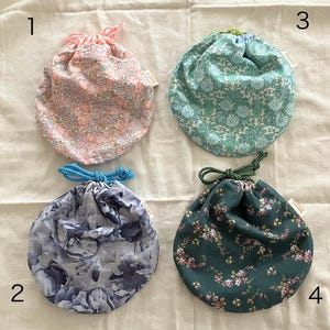 Puede incluir: Cuatro bolsas de tela con cordón de ajuste y diferentes estampados florales. Las bolsas están numeradas del 1 al 4.