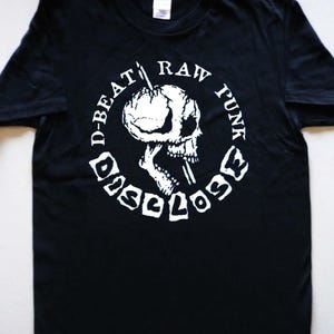 May include: Black t-shirt with a white graphic of a skull with a needle through its head. The graphic is surrounded by a circle with the text "D-BEAT RAW FUNK DISCLOSE".