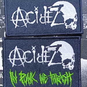 Op de afbeelding: Twee zwarte geborduurde patches met witte en groene letters. De bovenste patch zegt "ACID" met een schedelgrafiek. De onderste patch zegt "ACID" met een schedelgrafiek en de tekst "IN TUNK WE THRASH".