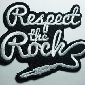 May include: White embroidered patch with the text "Respect the Rock" and a white audio jack on a black background.