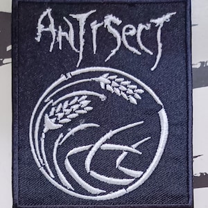 May include: A black embroidered patch with white stitching. The patch features the word "Antisect" in a stylized font and a circular design with wheat stalks and a wave-like pattern.