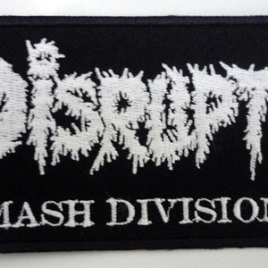 May include: Black rectangular patch with white embroidered text reading "DISRUPT" in a distressed font above "SMASH DIVISIONS". The patch is likely for clothing or accessories.