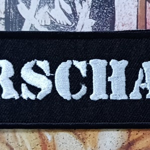 May include: A black fabric patch with the word "RORSCHACH" embroidered in white.