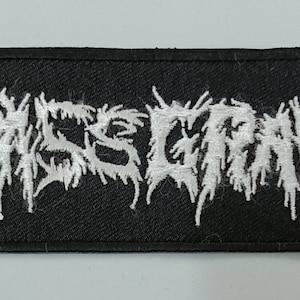 May include: White embroidered patch with the word "WARSCORN" in a stylized, jagged font on a black background.