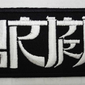 Peut inclure: Écusson brodé noir avec du texte blanc qui dit "鬼滅", qui est le mot japonais pour "Demon Slayer", et deux motifs de crânes blancs de chaque côté.