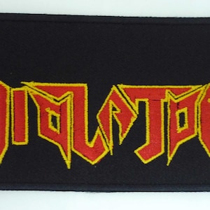 Może przedstawiać: Czarna naszywka haftowana z napisem "VIOLATOR" w czerwonych i żółtych literach. Litery są stylizowane z ostrymi kątami i szpicami.