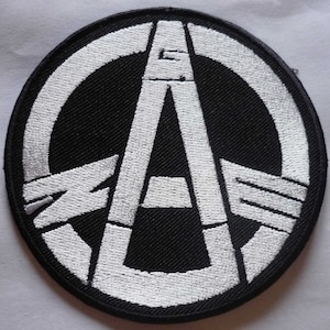 May include: A black and white embroidered patch with a peace sign symbol and the letter "A" inside. The peace sign is broken and the letter "A" is stylized.
