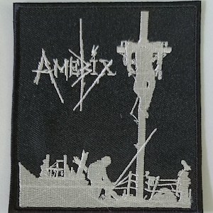 May include: A black and white embroidered patch with the word "Amebix" and a silhouette of a person on a cross.