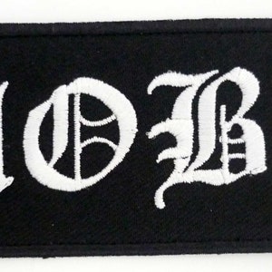 May include: A rectangular black patch with the white embroidered word "MOBS" in a gothic font. The patch has a black border and is likely designed to be sewn onto clothing or accessories.