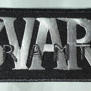 Peut inclure: Un écusson rectangulaire noir brodé avec le mot "SVART" en grandes lettres argentées stylisées. En dessous, le mot "RAMP" est brodé en plus petit. L'écusson a une bordure argentée.