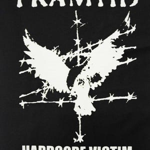 May include: Black graphic tee with the word "FRAMTID" at the top and "HARDCORE VICTIM" at the bottom. A white graphic of a bird with outstretched wings is in the center, with barbed wire and star-like shapes.