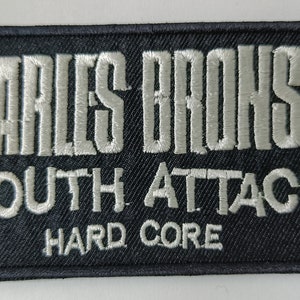 Könnte beinhalten: Schwarzer gestickter Aufnäher mit weißem Text, der "Charles Bronson Youth Attack! Hard Core" lautet.