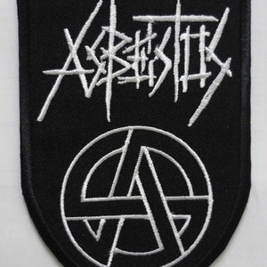 以下が含まれることがあります： 「X-KASTIX」というテキストとアナーキーシンボルが刺繍された黒と白のパッチ