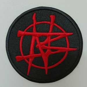 Puede incluir: Parche bordado rojo con un símbolo estilizado dentro de un círculo sobre un fondo negro.