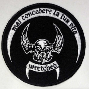 Può includere: Una toppa ricamata in bianco e nero con un design di teschio e ali. Il testo "Wretched" è sotto il teschio e il testo "mai concedere la tua vita" è in un cerchio attorno al teschio.