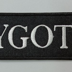 May include: Black embroidered patch with white text that reads "YGOTE." A white symbol with arrows is to the left of the text.