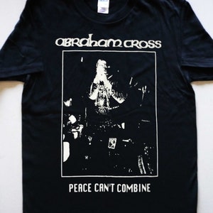 Peut inclure: T-shirt noir avec un imprimé graphique blanc d'une personne dans un groupe. Le texte "abraham cross" et "peace can't combine" sont imprimés sur le t-shirt.