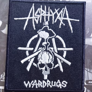 Peut inclure: Un écusson carré noir avec des broderies blanches. Le mot "Asphyxa" est inscrit en arc de cercle en haut. En dessous, un crâne avec des armes croisées et le mot "WARDRUGS" en bas. Idéal pour personnaliser un vêtement.