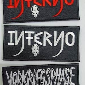 Peut inclure: Trois écussons rectangulaires noirs avec texte brodé. Le patch supérieur indique "Inferno" en rouge avec un motif de crâne. Le patch du milieu indique "Inferno" en blanc avec un motif de crâne. Le patch inférieur indique "Vorkriegsphase Auf In Den Tod" en blanc.